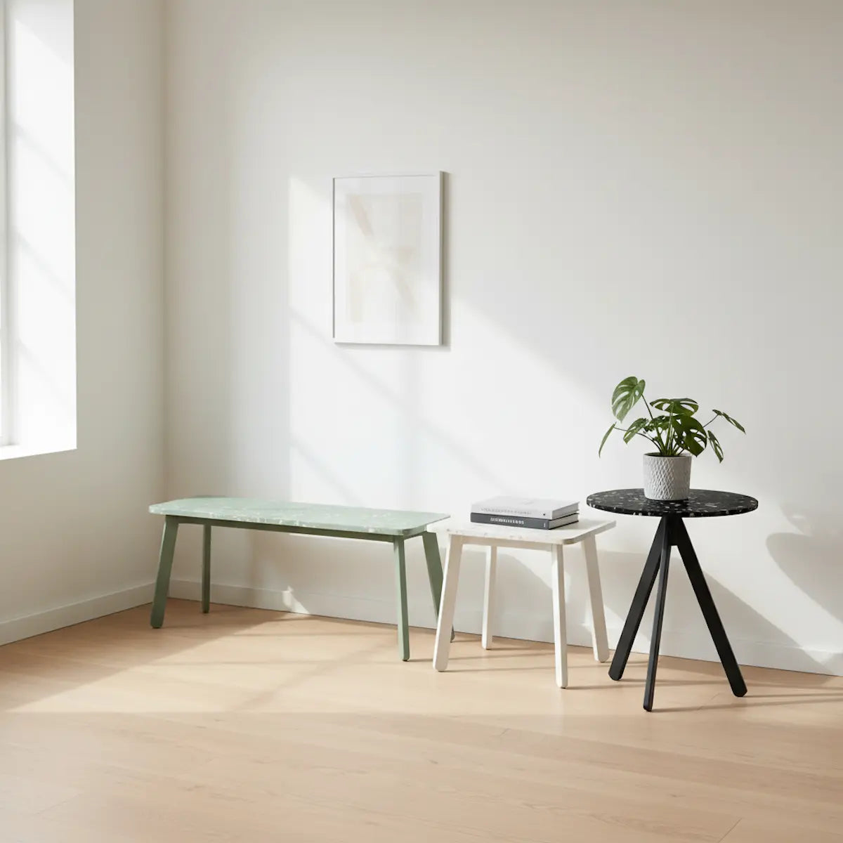 Recycled plastic terrazzo furniture collection featuring a rectangular bench in moss green, square side table in chalk white, and round side table in basalt black, styled in a Scandinavian interior.