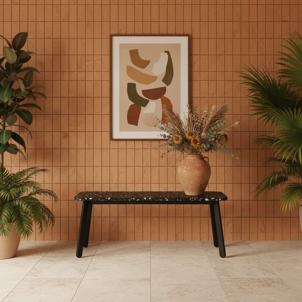 Black recycled plastic bench with terrazzo-effect panel top against a terracotta tiled wall, styled with a dried flower vase and framed abstract art