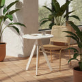 White HDPE table with tripod base on a terrace, paired with a gold-legged rattan chair and surrounded by potted plants