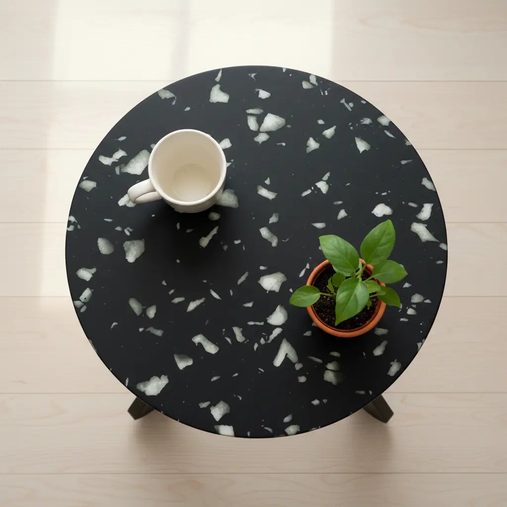 Top view of a black HDPE side table with white speckled panel pattern, holding a coffee mug and small potted plant