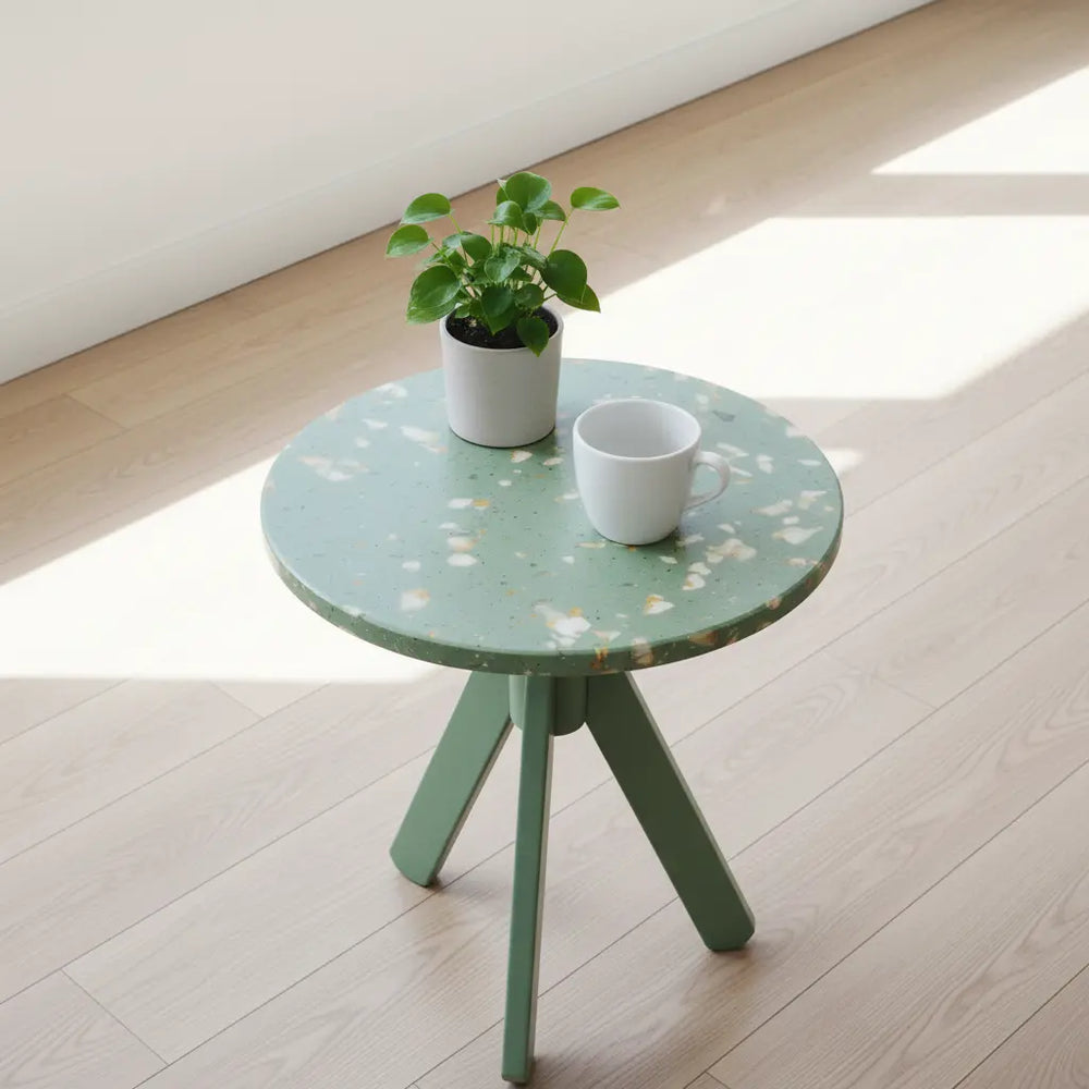 Green eco-friendly side table made from recycled polymer, with tripod legs, a potted plant, and white mug, set on a wood floor